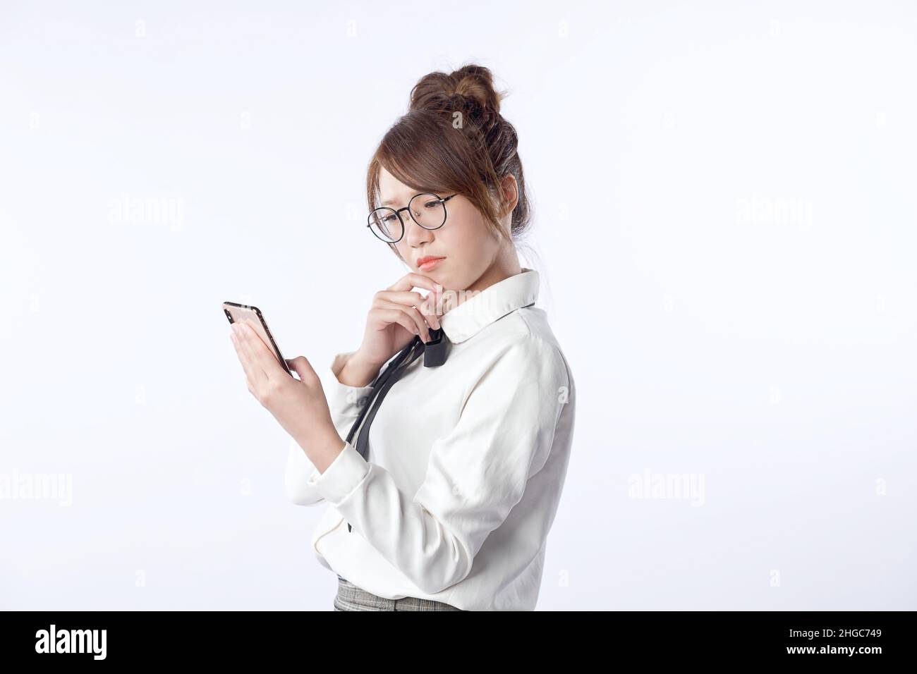 Porträt eines jungen Mädchens, das ein Handy in der Hand hält und sich um etwas mit isoliertem weißem Hintergrund sorgt. Negative Gesichtsausdruck der menschlichen Emotion Stockfoto