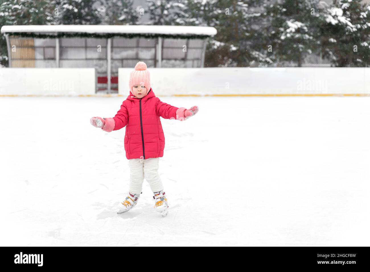 Das kleine Mädchen in einer roten Jacke ist auf der Eisbahn Schlittschuh Stockfoto