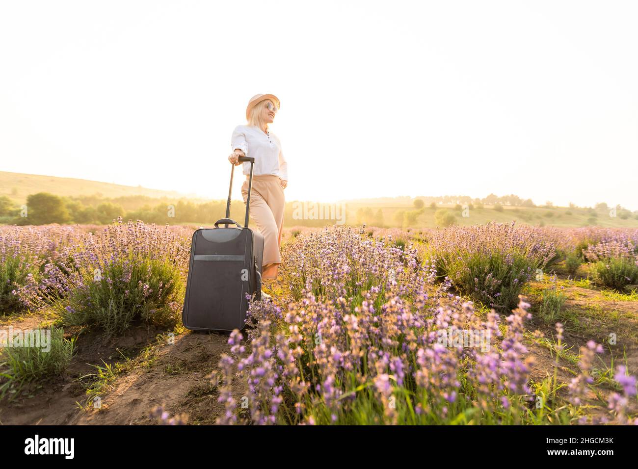 Frau mit Koffer in der Hand in einem Lavendelfeld am Sommernachmittag Stockfoto