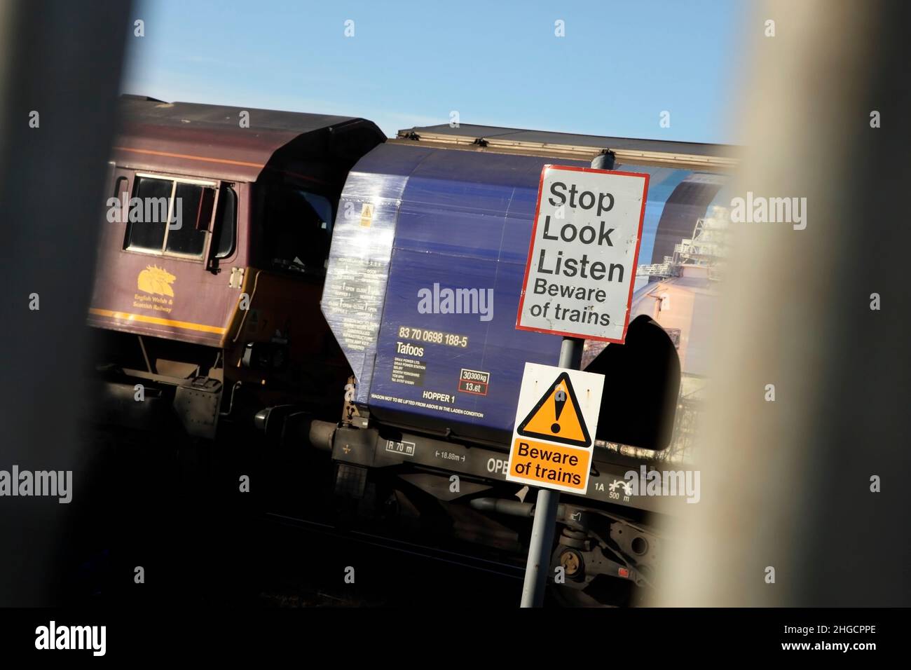 Warnschilder auf der Gleisseite neben dem vorbeifahrenden Güterzug, der von der Lokomotive der Klasse 66 66007, Scunthorpe, Großbritannien, gezogen wird. Stockfoto
