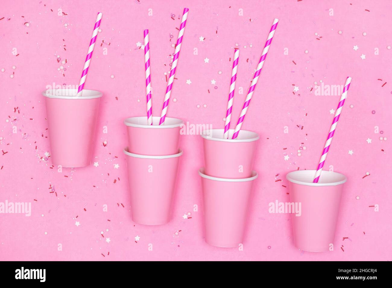 Pinke Pappbecher mit gestreiften Trinkhalmen und Süßigkeitenstreuseln auf rosa Hintergrund. Girly Party, Sweet Beverage Konzept Stockfoto
