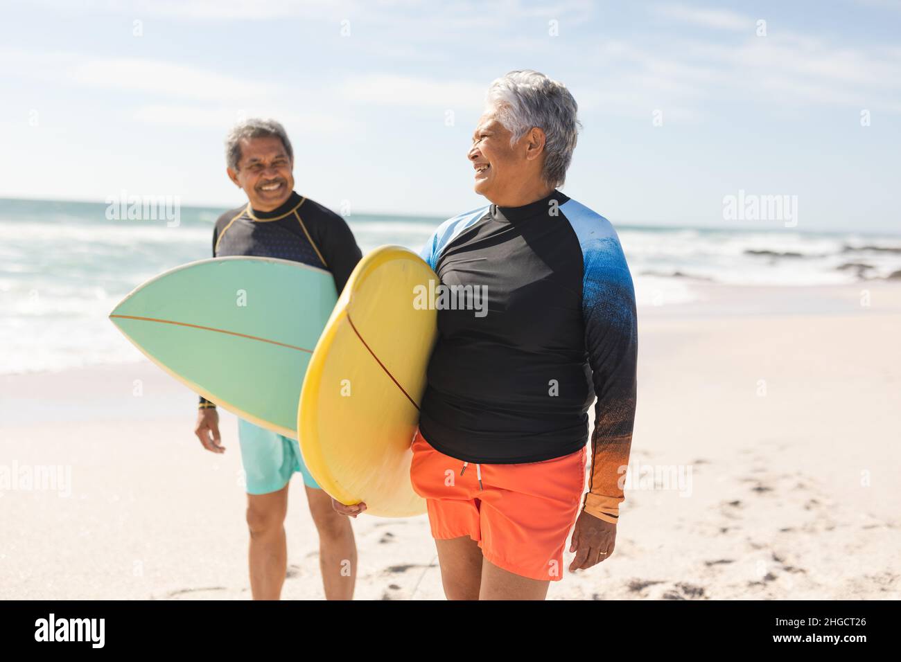 Lächelndes, multirassisches Seniorenpaar, das sich an sonnigen Tagen mit Surfbrettern an Land ansieht Stockfoto