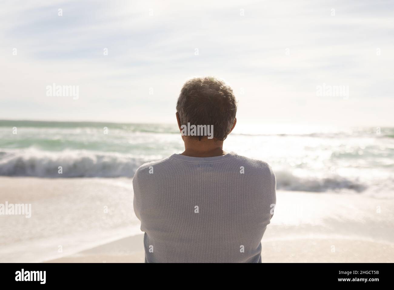 Rückansicht eines älteren Biracial-Mannes, der vom sonnigen Strand aus Wellen vom Meer gegen den Himmel schaue Stockfoto