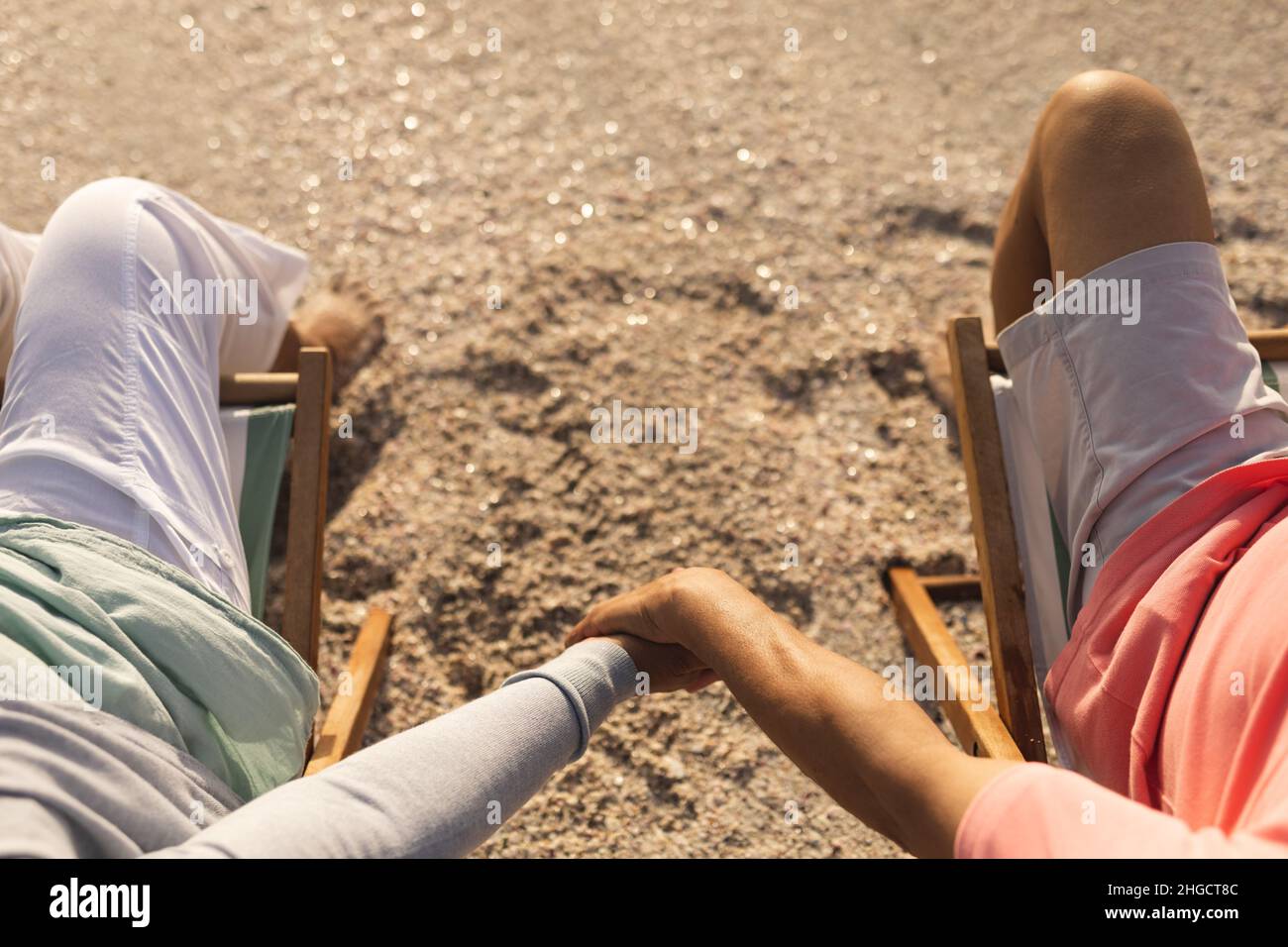 Blick aus der Perspektive eines mehrrassigen älteren Ehepaares, das die Hände hält, während es sich auf den Stühlen am Strand entspannt Stockfoto