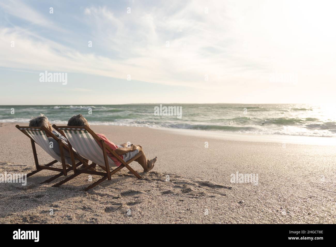 Ältere Männer und Frauen aus dem Biracial entspannen sich, während sie am Strand auf Klappstühlen sitzen Stockfoto