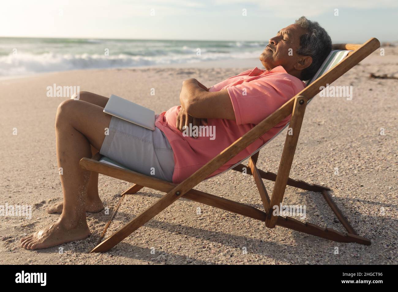 Seitenansicht eines älteren Birazialmannes mit Laptop, der auf einem Klappstuhl schlief und sich am Strand entspannen konnte Stockfoto