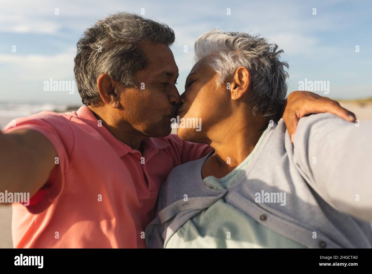 Romantisches mehrrassiges Senior-Paar, das sich beim Selfie am Strand küsst Stockfoto