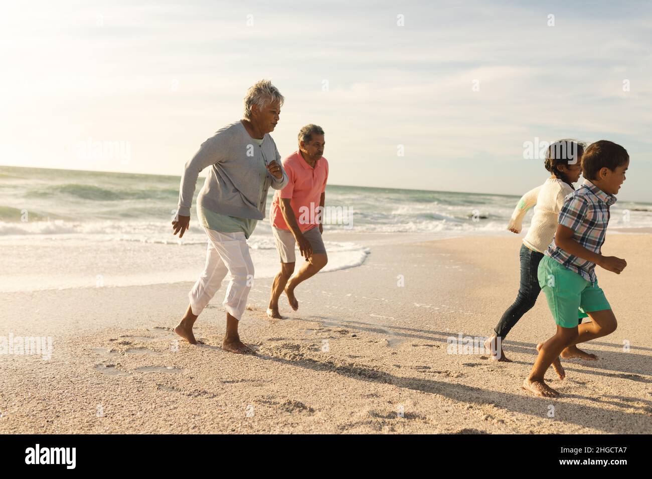 Multirassische Großeltern, die am Strand gegen den Himmel hinter Enkelkindern laufen Stockfoto
