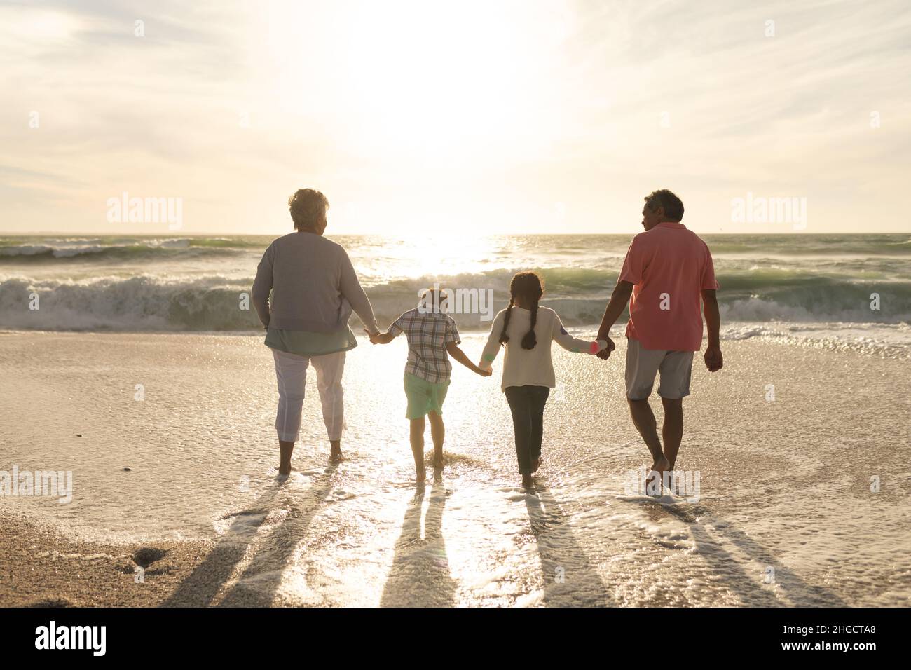 Die ganze Länge der multirassischen Großeltern und Enkelkinder hält die Hände, die am Strand zusammenlaufen Stockfoto