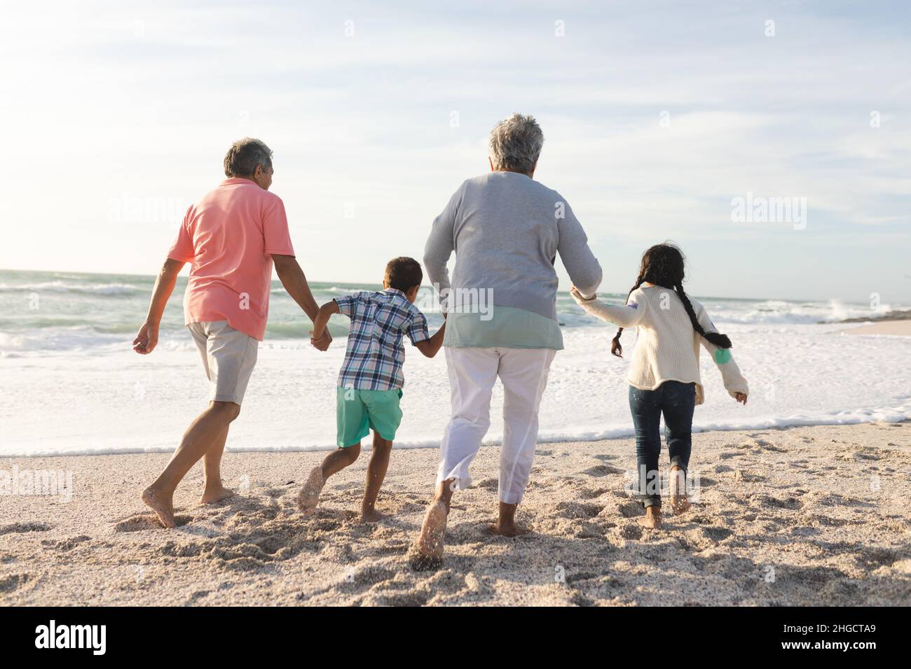 Rückansicht von älteren Großeltern verschiedener Rassen, die mit Enkelkindern am Strand entlang gehen Stockfoto
