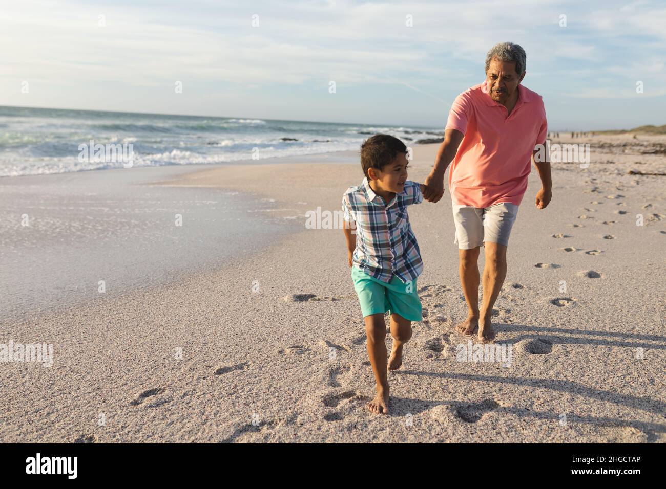 Die ganze Länge des Biracial Jungen hält Hand ziehen Großvater, während am Strand gegen den Himmel zu Fuß Stockfoto