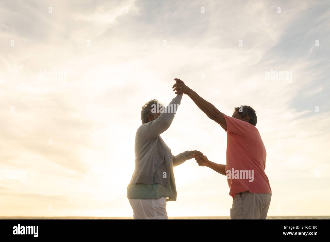 Low-Angle-Seitenansicht Senior multiracial Paar genießen Tanz am Strand gegen Himmel während des Sonnenuntergangs Stockfoto