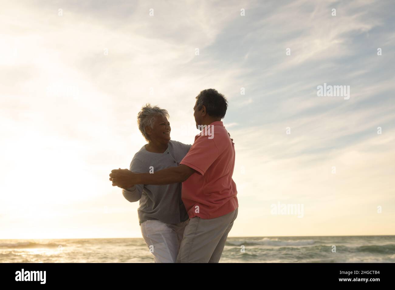 Glückliches Senioren-Paar, das während des Sonnenuntergangs romantisch am Strand gegen den Himmel tanzt Stockfoto