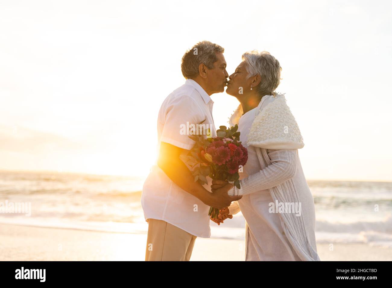 Seitenansicht eines mehrrassigen älteren Ehepaares, das sich während der Hochzeitszeremonie am Strand küsst Stockfoto