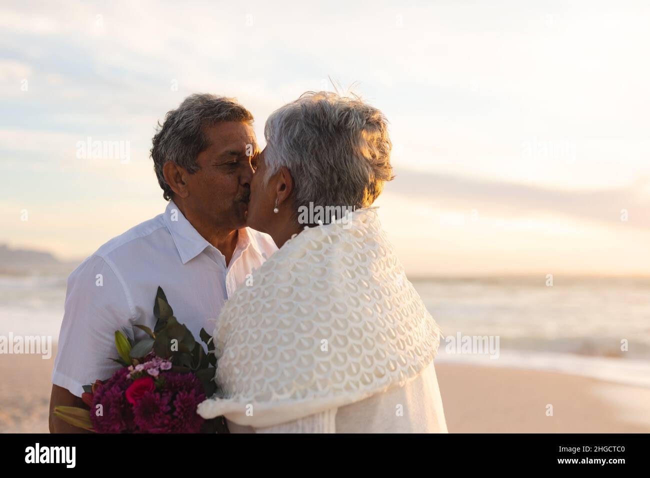 Das frisch vermählte ältere multirassische Paar küsste sich während der Hochzeitszeremonie am Strand Stockfoto