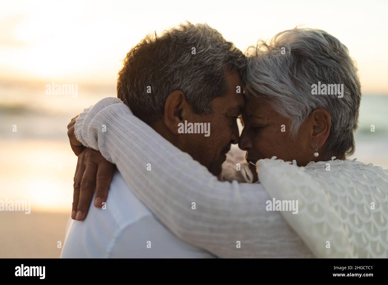 Seitenansicht des liebevollen jungen Biracial Senior Braut und Bräutigam umarmen während des Sonnenuntergangs Stockfoto