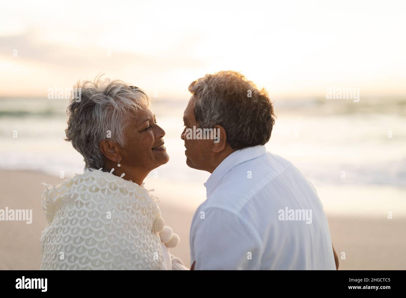Seitenansicht eines glücklichen, multirassischen Seniorenpaares, das sich während des Sonnenuntergangs romantisch ansah Stockfoto