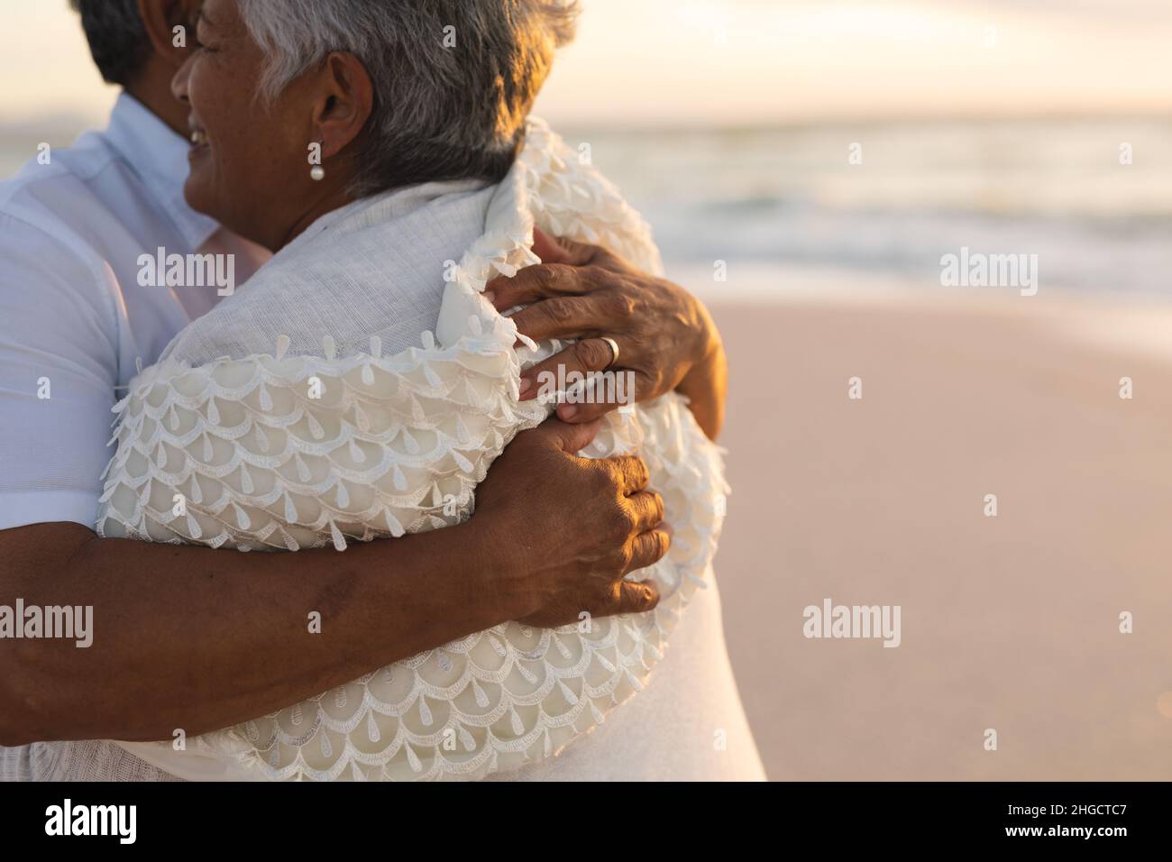 Mittelteil eines frisch vermählten mehrrassischen älteren Ehepaares, das sich am Strand während des Sonnenuntergangs umarmte Stockfoto