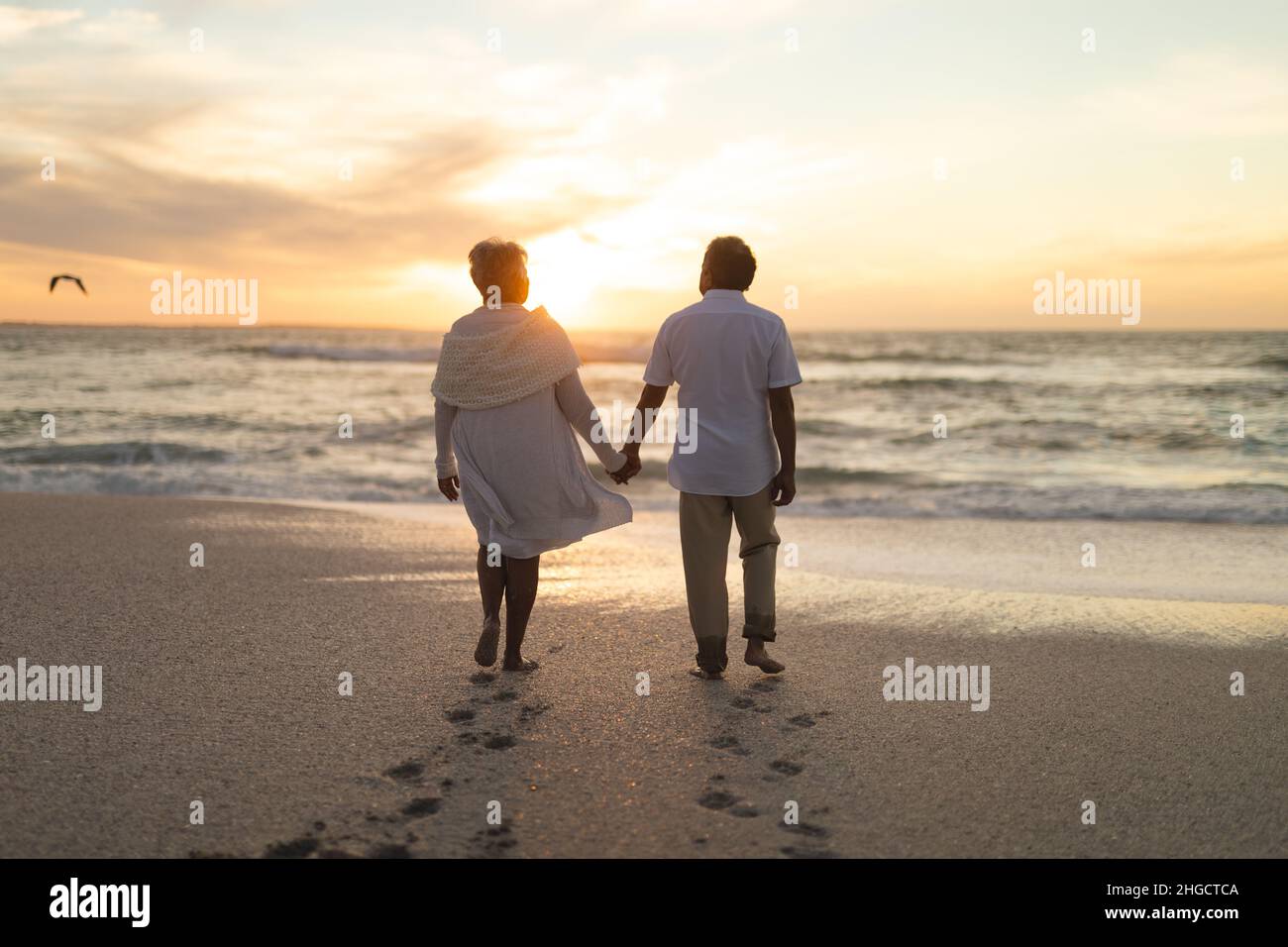 Die gesamte Länge eines jungen mehrrassischen Ehepaares, das während des Sonnenuntergangs zum Strand läuft Stockfoto