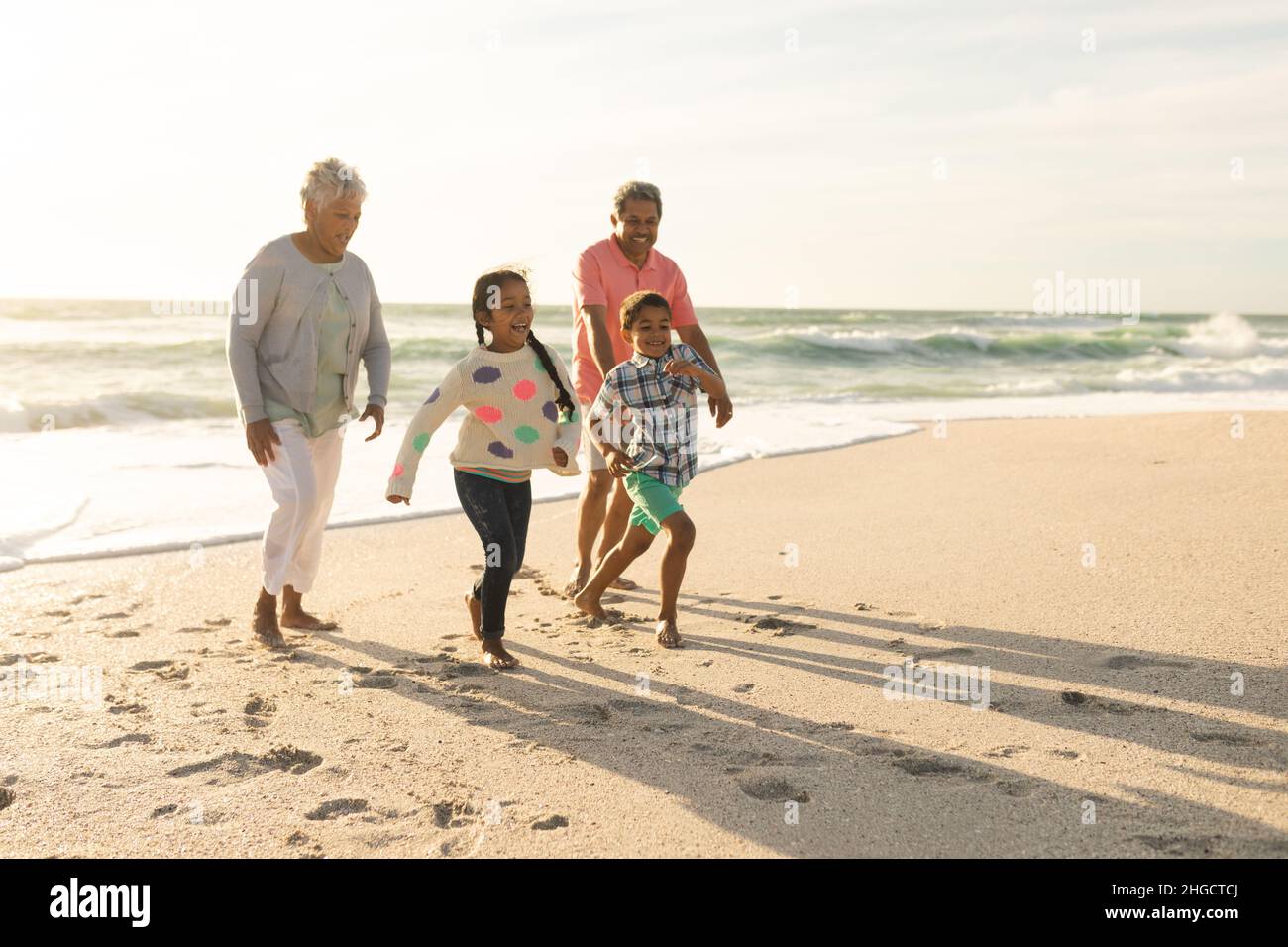 Multirassische Enkelkinder mit Großeltern, die während des Sonnenuntergangs am Strand gegen den Himmel spazieren Stockfoto