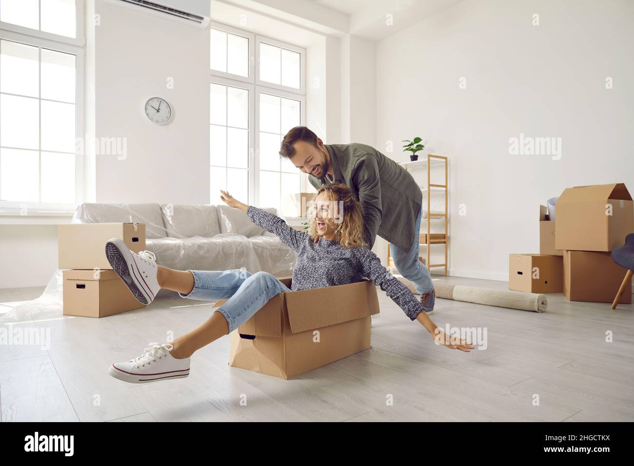 Glückliches junges Ehepaar, das am Umzugstag mit Pappkartons in einem neuen Zuhause Spaß hat. Stockfoto