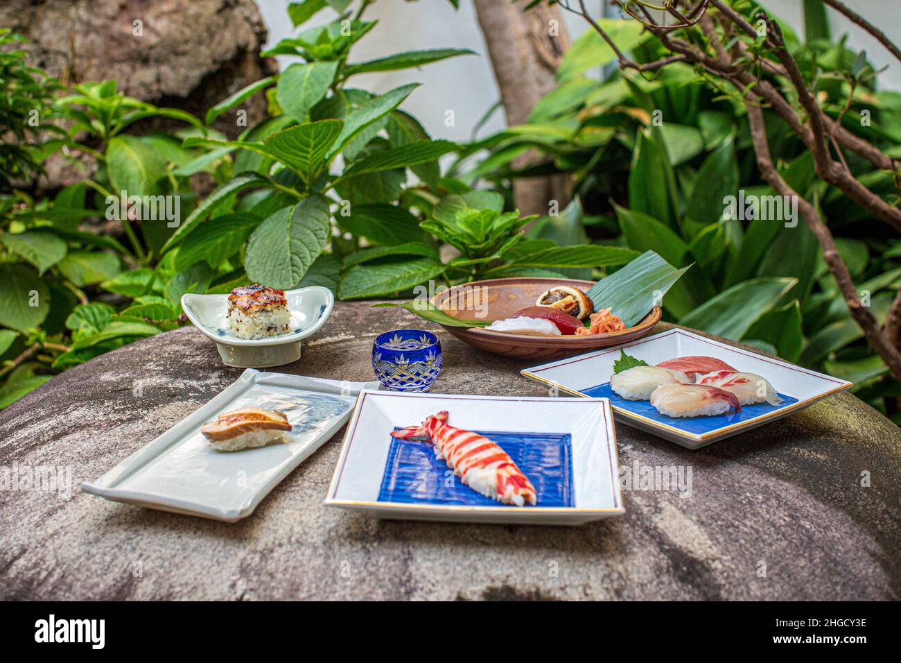 Sushi-Set und Sashimi mit Sake auf grauem Stein serviert mit Garten im Hintergrund. Stockfoto