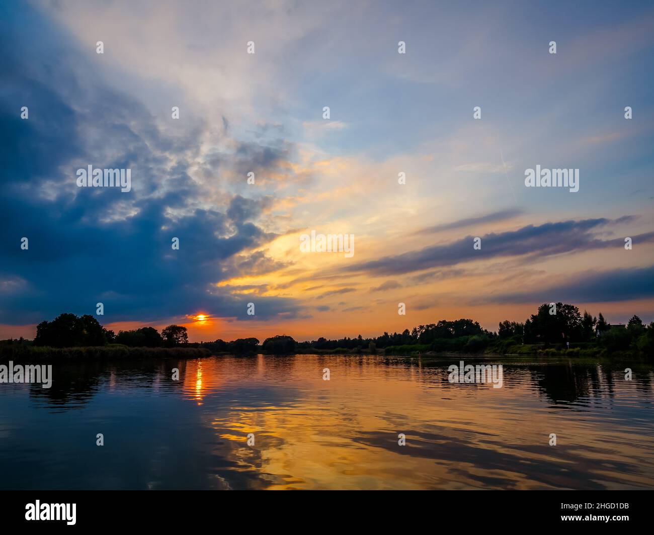 Abendhimmel mit dramatischen Wolken über dem Fluss. Dramatischer Sonnenuntergang in Wolken und Fluss. Naturlandschaft, Reflexion, blauer wolkig Himmel und orange Sonnenlig Stockfoto