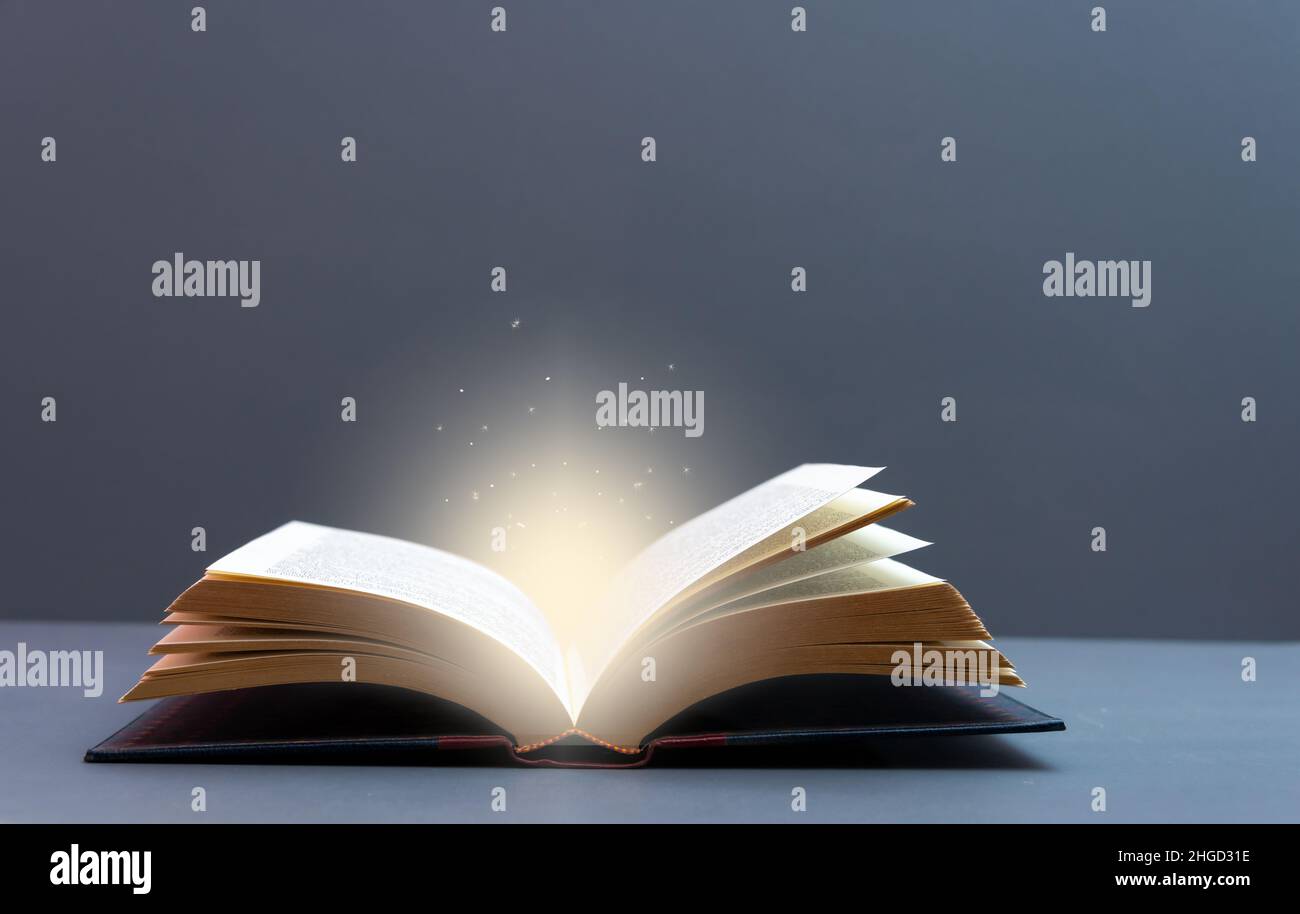 Mystery offenes Buch mit leuchtendem Licht. Fantasy-Buch mit magischem Licht und Sternen auf einem Tisch mit grauem Hintergrund und Kopierraum Stockfoto