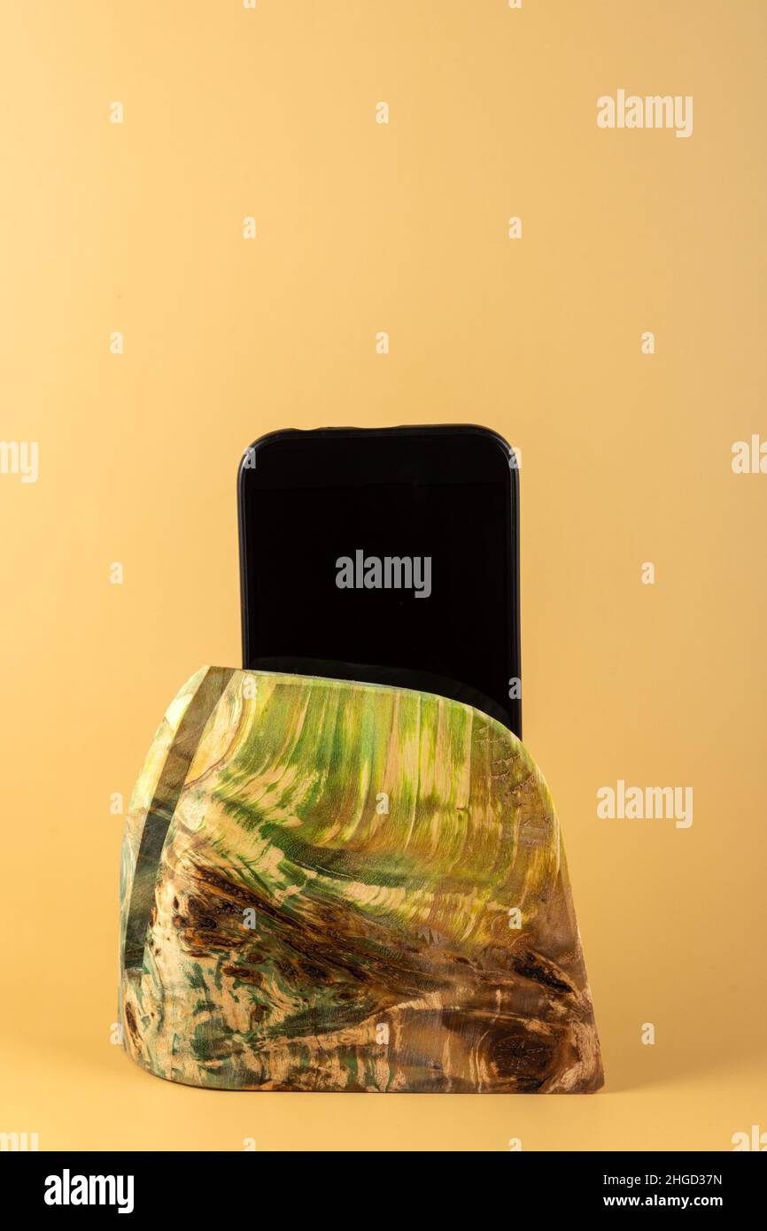 Smartphone in einem Ständer aus stabilisiertem Ahornholz auf gelbem Hintergrund. Speicherplatz kopieren Stockfoto
