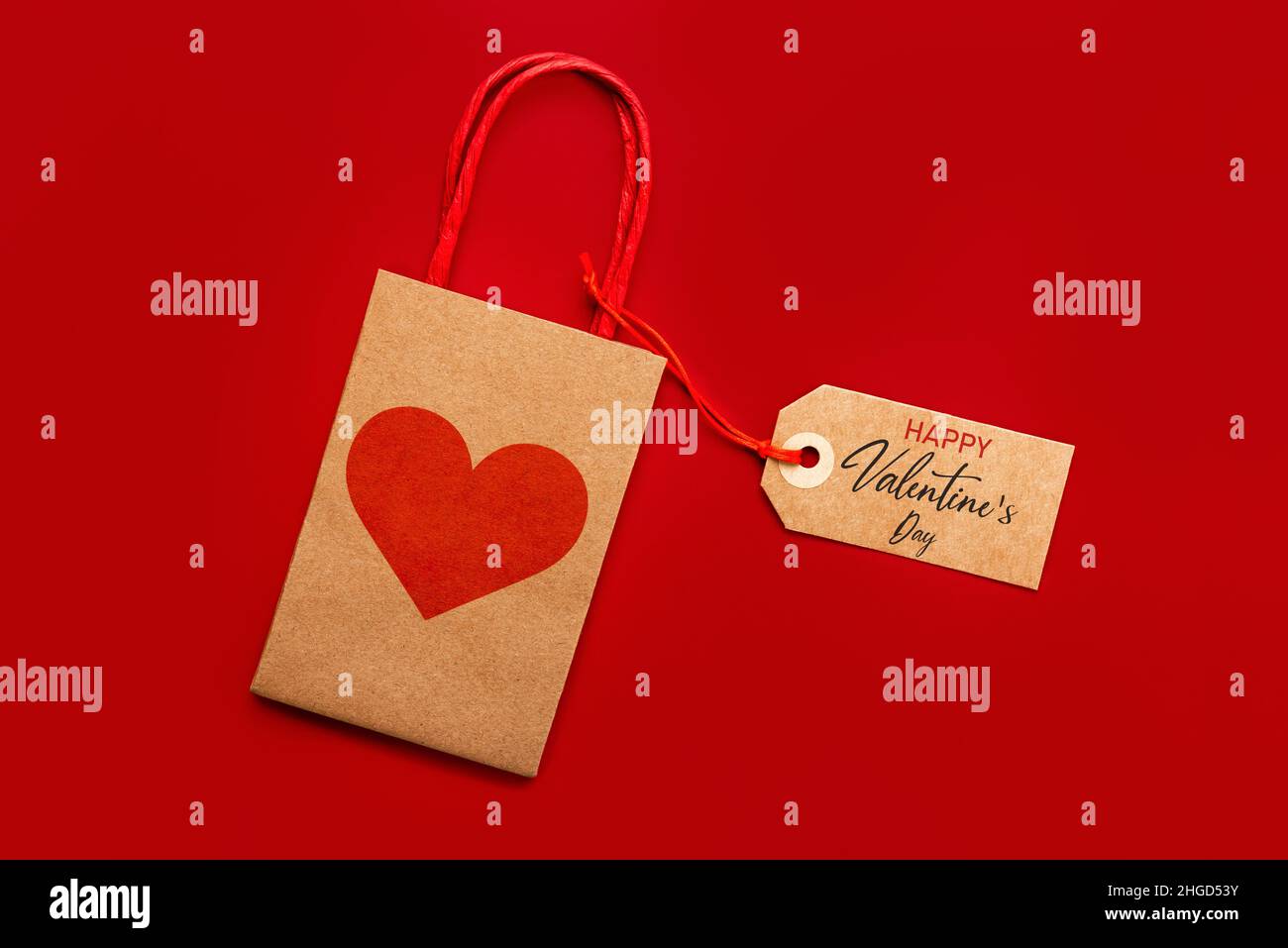 Draufsicht auf Einkaufstasche mit rotem Herz und braunem Sale-Tag mit Text Happy Valentine's day auf rotem Hintergrund. Konzept für die Valentinstag-Feier Stockfoto