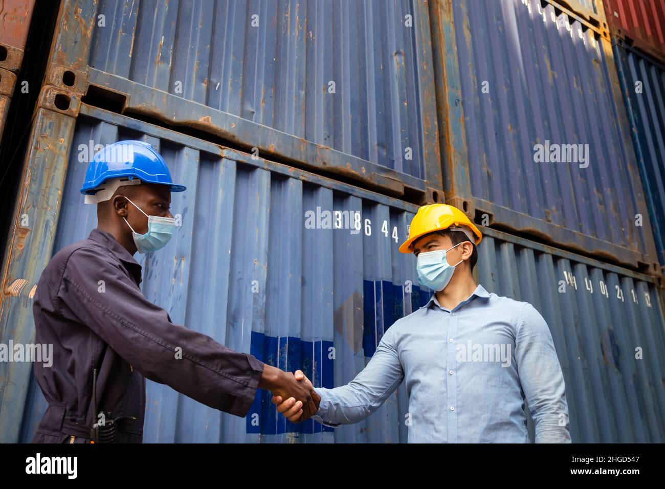 afrikanischer Arbeiter und kaukasischer Geschäftsmann mit Gesichtsmaske zum Schutz vor Covid- oder Coronaviren schütteln sich nach dem Suc im Frachtlager die Hand Stockfoto