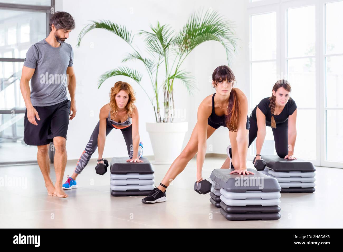 Fitnesstrainerin mit einer Klasse von Athleten in einem Fitnessstudio, die Gewichtheben mit Hanteln, um ihre Körpermuskulatur und den inneren Kern in einer Gesundheit zu stärken Stockfoto