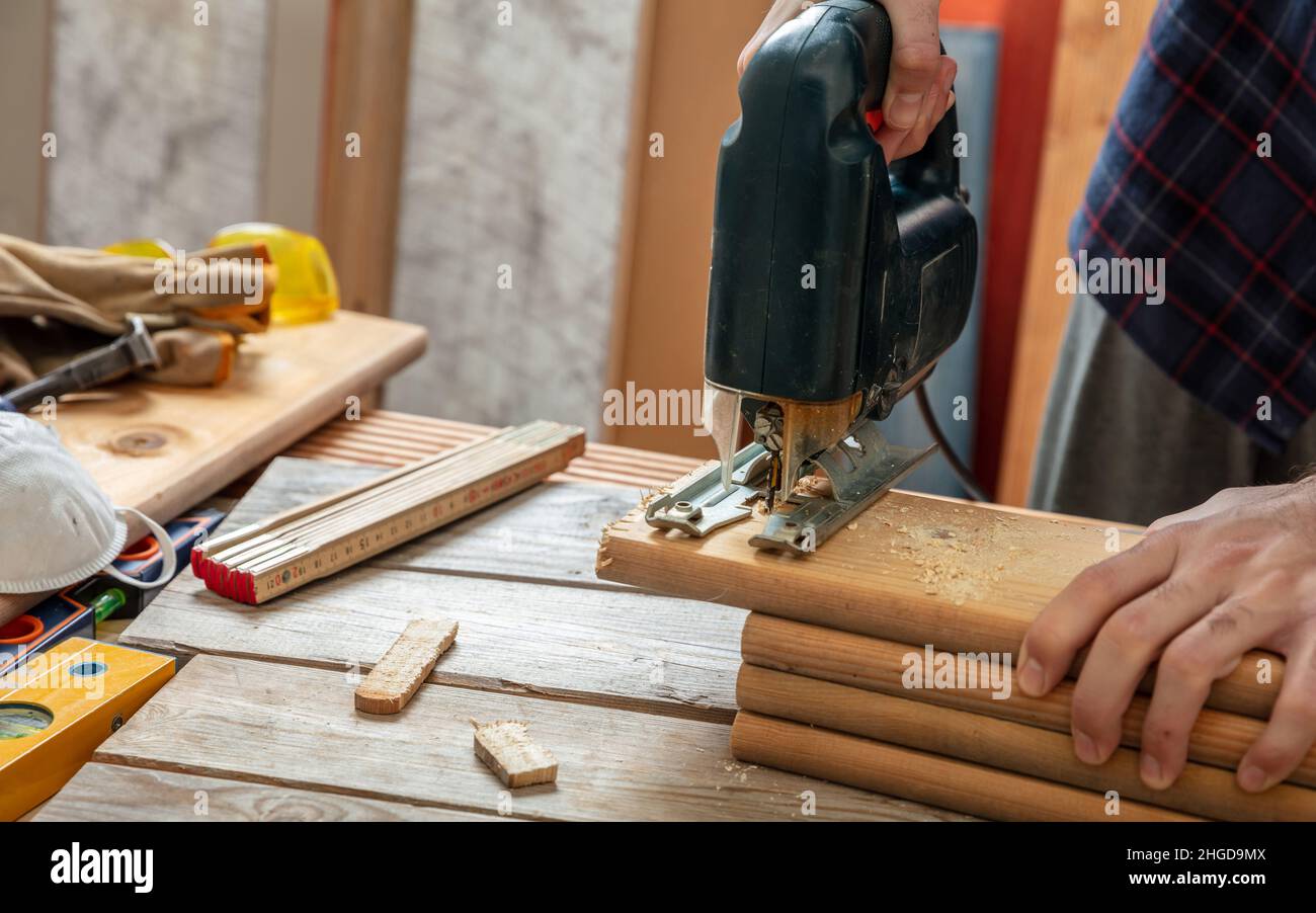 Elektrische Stichsäge, Zimmermann, der Holz mit einer elektrischen Säge von Hand schneidet. Bauindustrie, Nahaufnahme des Arbeitstisch-Tisches Stockfoto