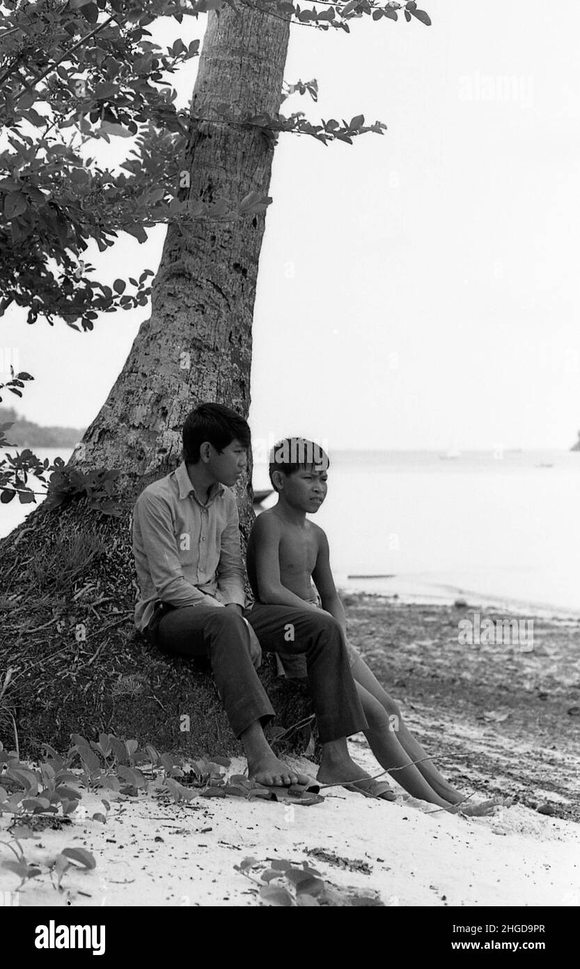 Ein paar junge Singporäer bei einer Palme träumen von einem zukünftigen Singapur an einem Strand im Jahr 1967 Stockfoto