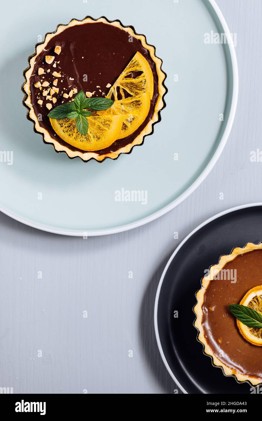 Schokoladentörtchen auf grauem Hintergrund, verziert mit Minzblättern und getrockneter Orange Stockfoto