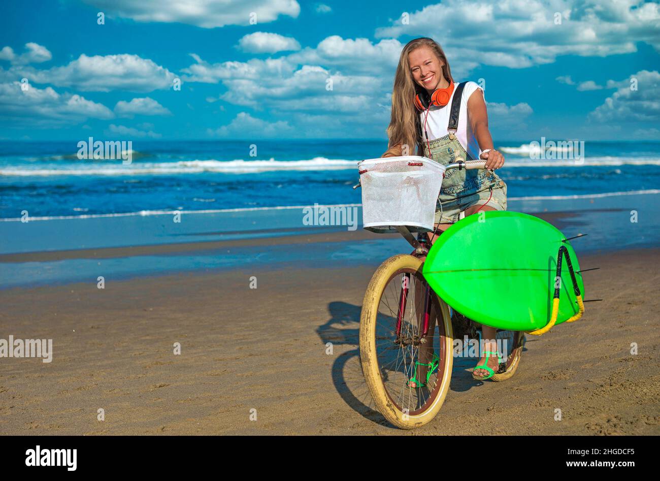 Junge Frau mit Surfbrett und Fahrrad am Strand. Stockfoto