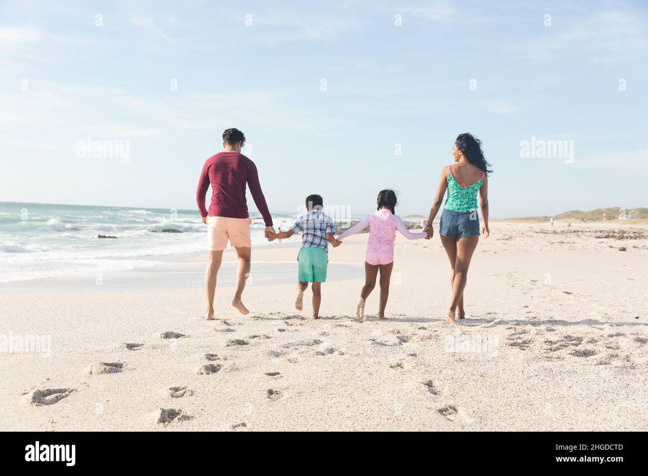 Die ganze Familie hält die Hände zusammen und läuft auf Sand mit Fußabdrücken am Strand Stockfoto