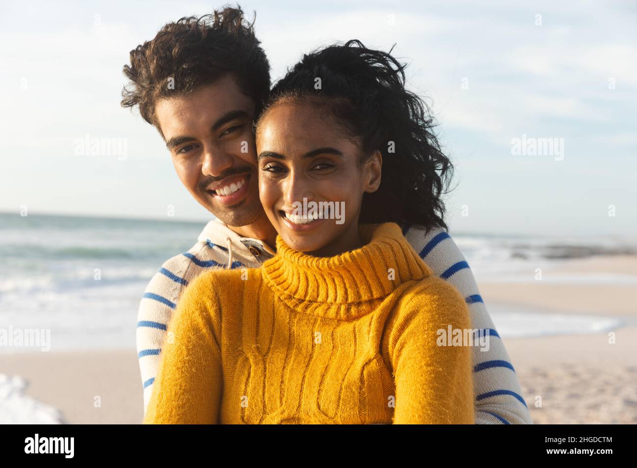Porträt eines lächelnden multirassischen Paares, das an einem sonnigen Tag am Strand gegen den Himmel steht Stockfoto