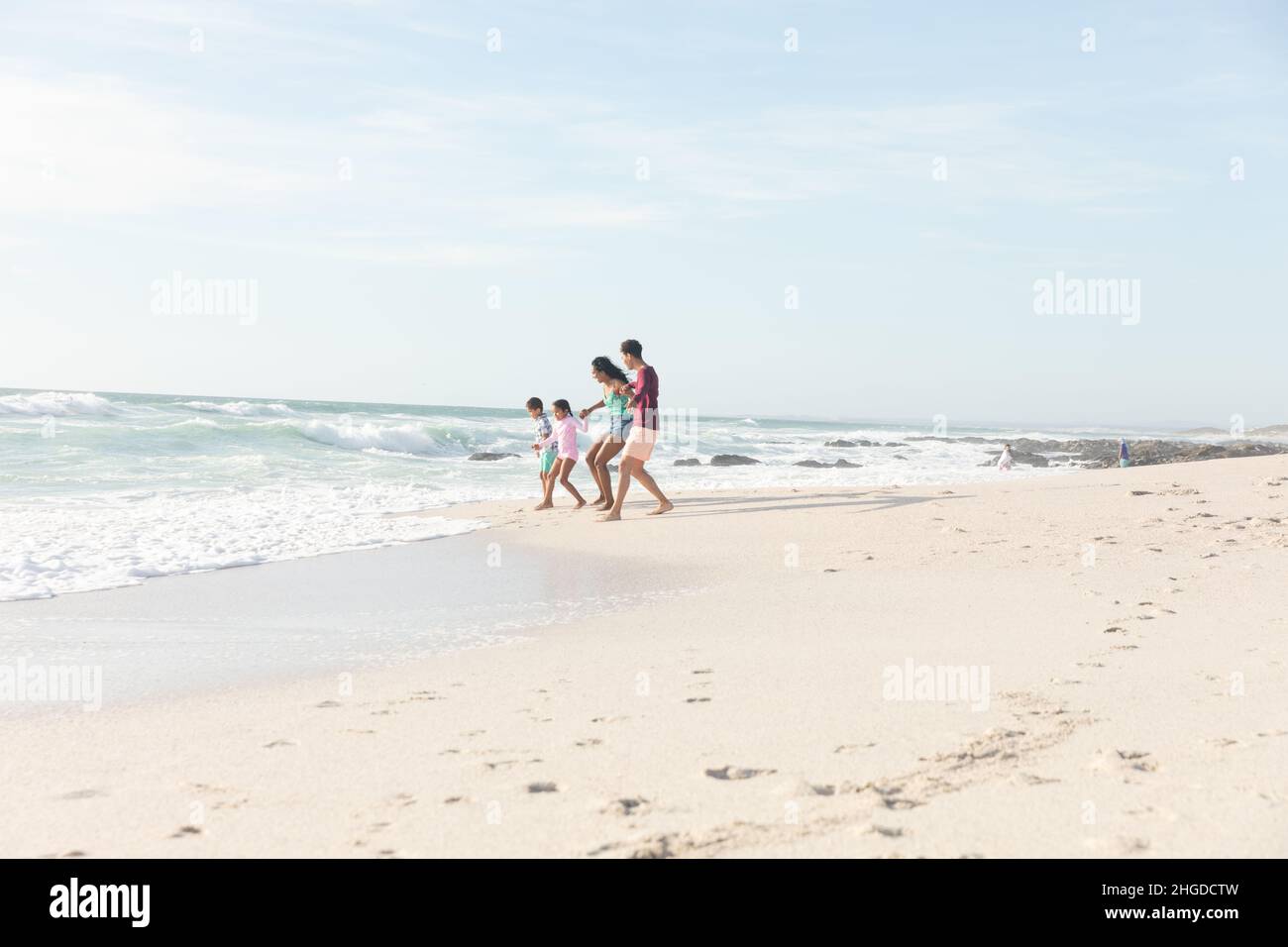 Die gesamte Länge der multirassischen Familie, die an sonnigen Tagen am Strand gegen den Himmel am Ufer zusammenläuft Stockfoto