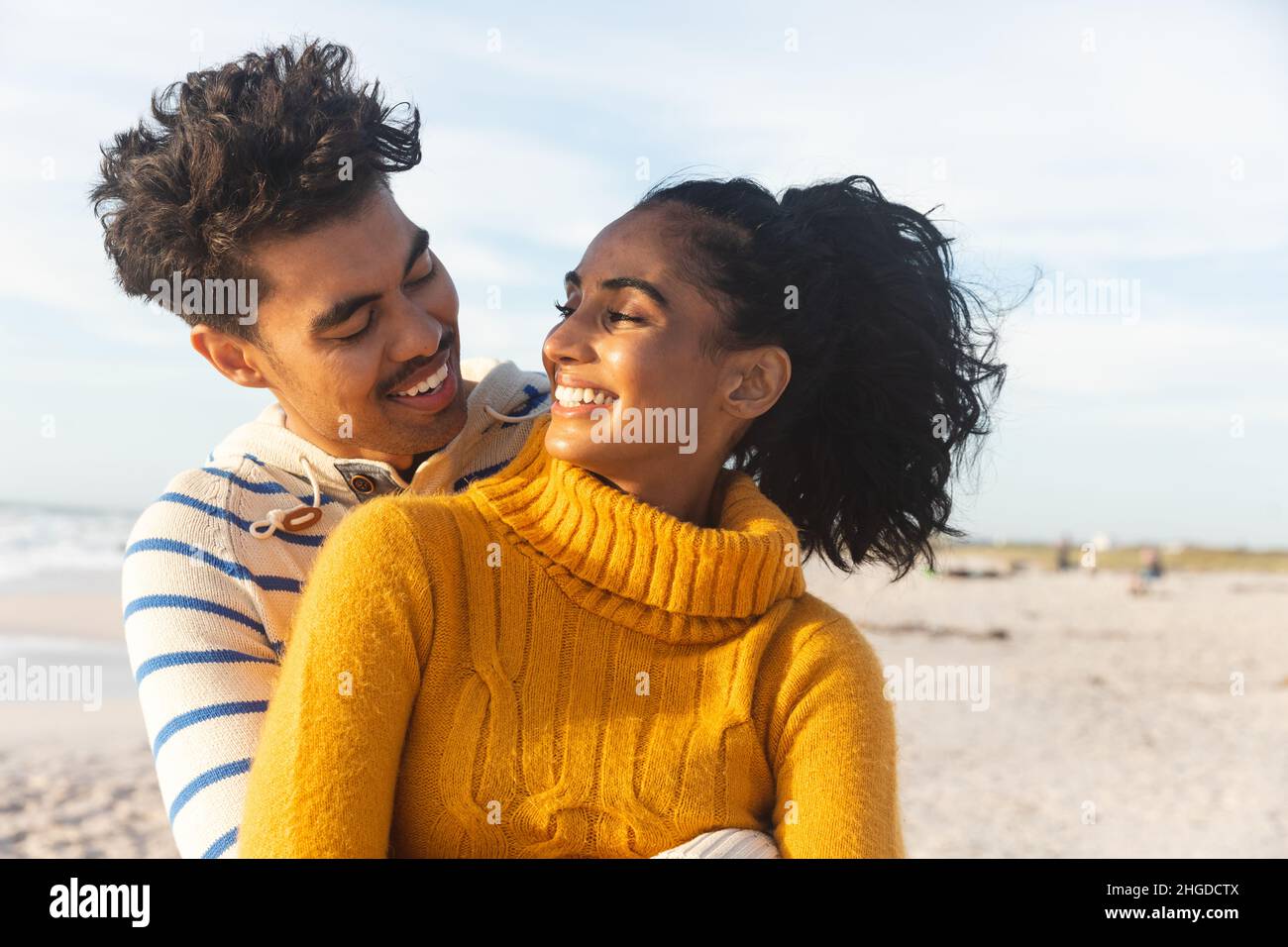 Lächelndes, multirassisches Paar, das sich anschaut, während es den sonnigen Tag am Strand genießt Stockfoto