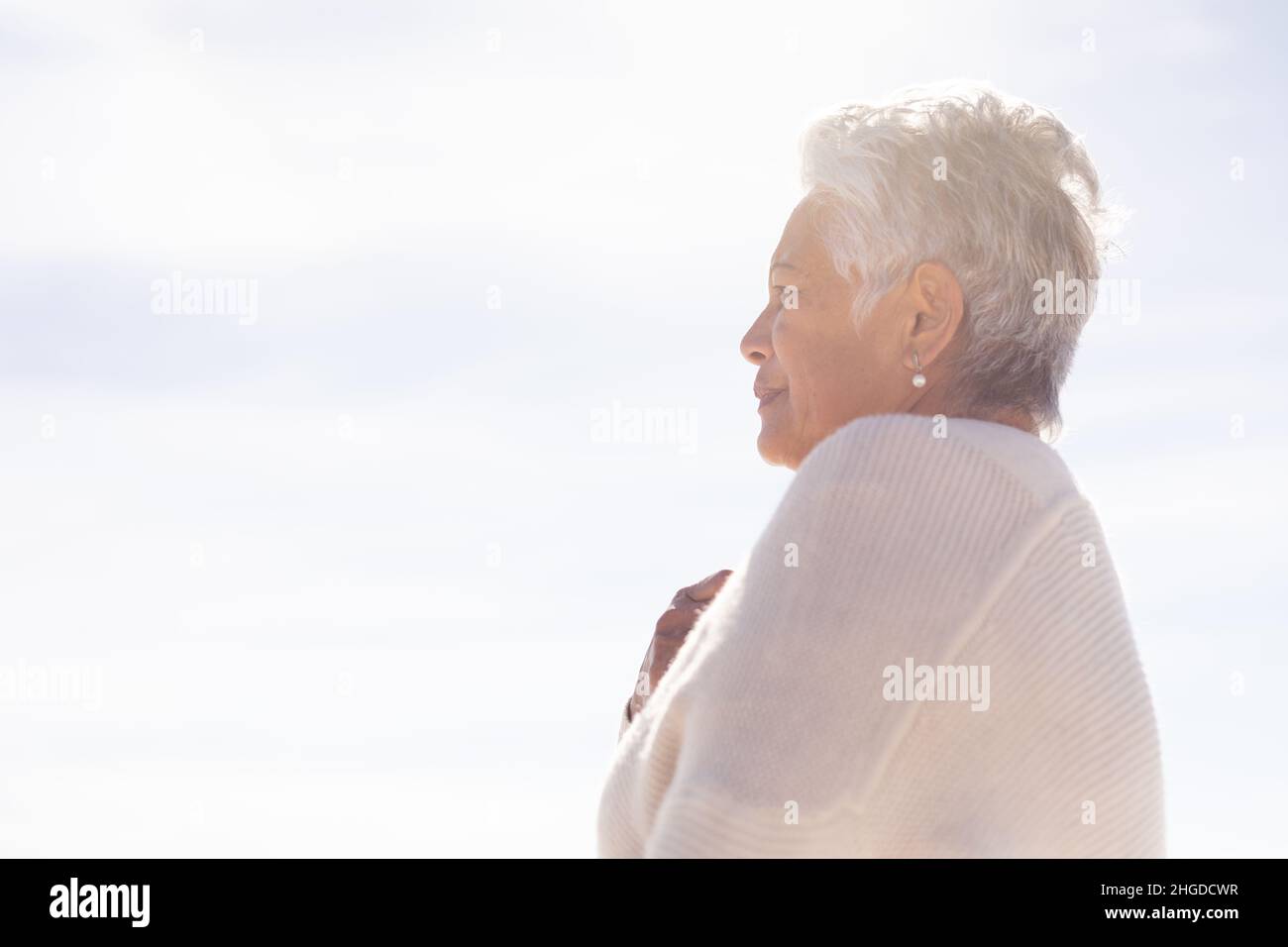 Flache Seitenansicht einer älteren Birazialfrau, die während eines sonnigen Tages am Strand steht und wegschaut Stockfoto