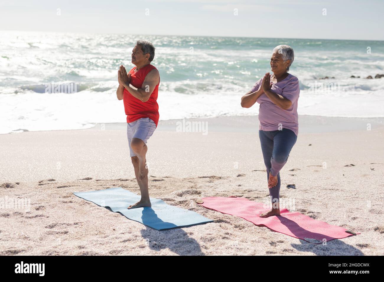Das Seniorenpaar, das an sonnigen Tagen am Strand Yoga auf Übungsmatten praktiziert, übt Baum Stockfoto