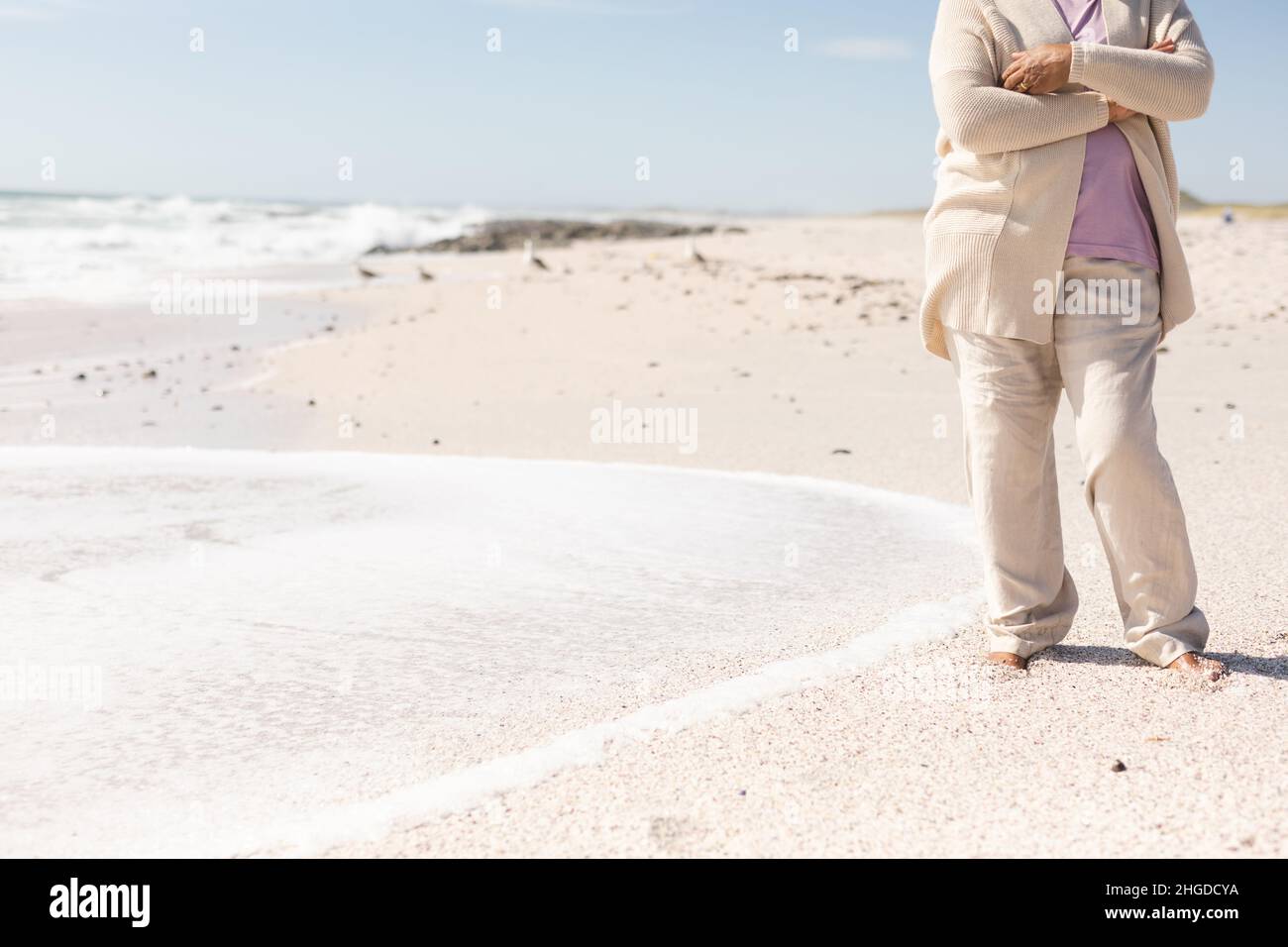 Niedriger Abschnitt einer älteren Birazialfrau, die an sonnigen Tagen mit gekreuzten Armen am Strand steht Stockfoto
