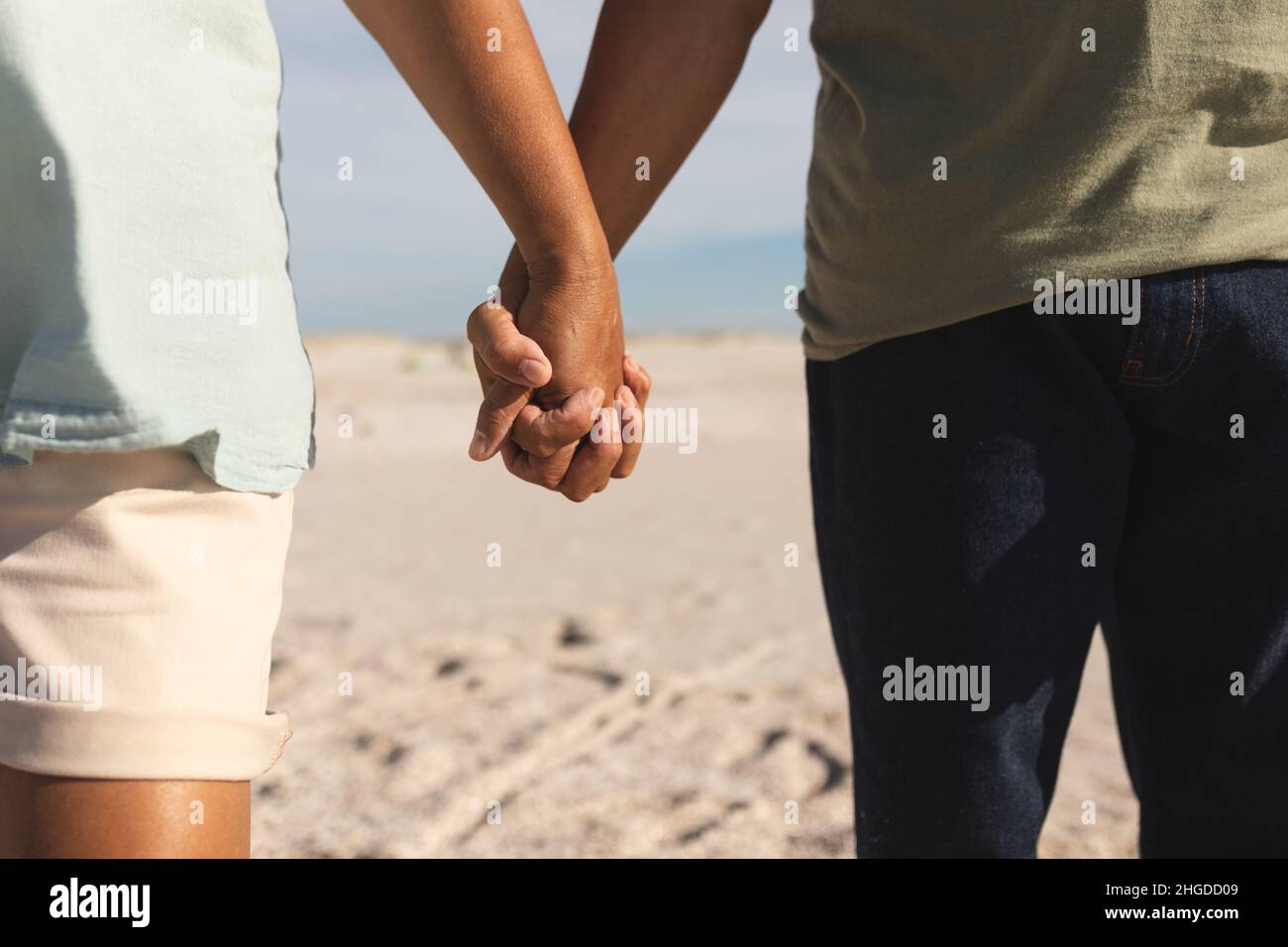Mittelteil eines mehrrassischen älteren Ehepaares, das an sonnigen Tagen die Hände am Strand zusammenhält Stockfoto