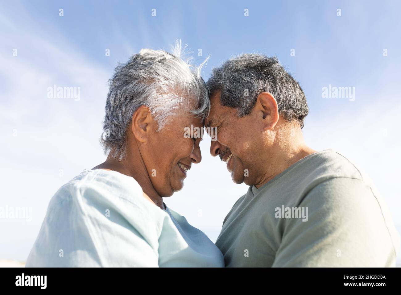 Seitenansicht eines lächelnden mehrrassischen älteren Ehepaares, das während eines sonnigen Tages die Stirn am Strand berührte Stockfoto