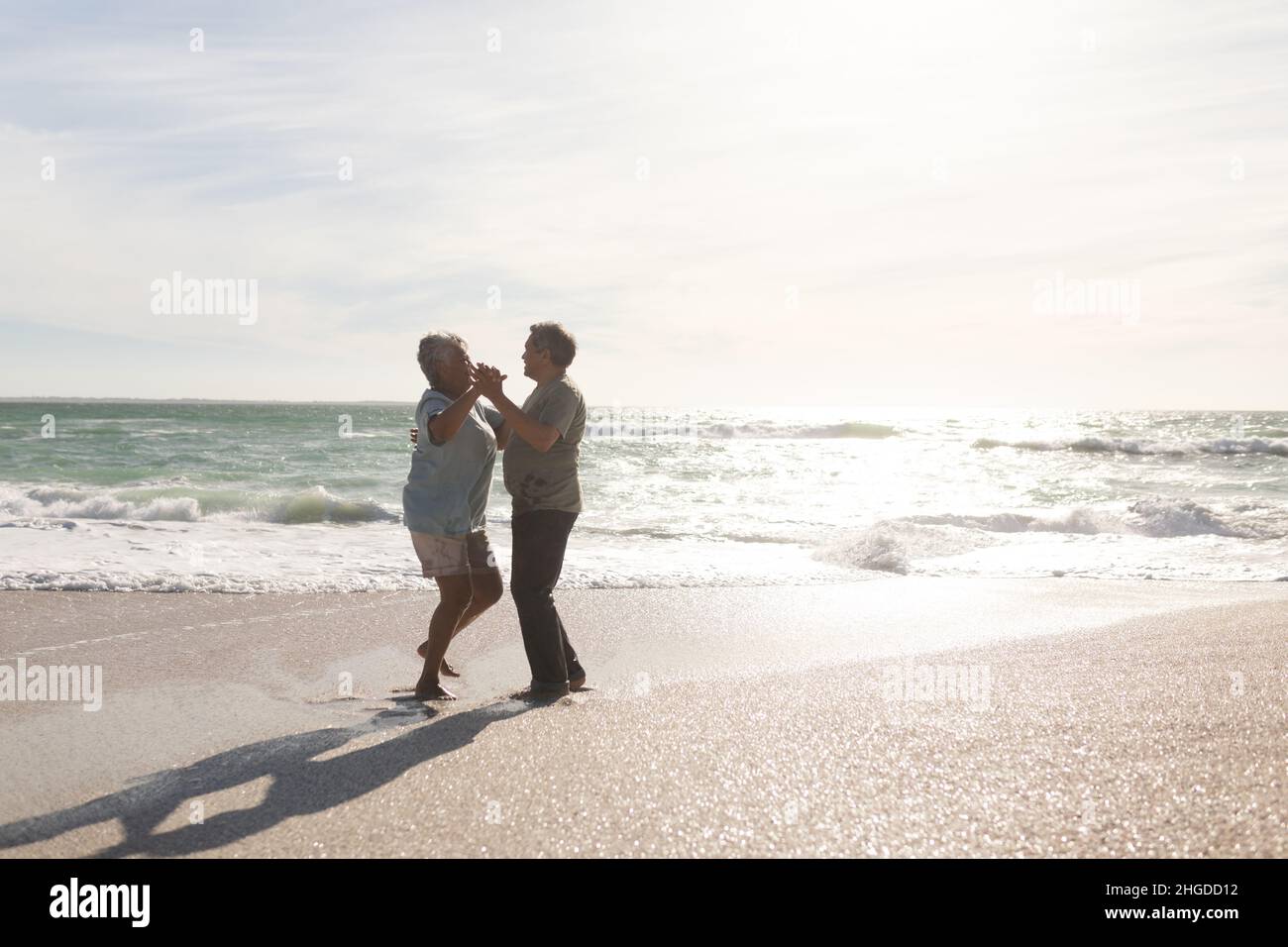 Ganztägige Seitenansicht eines glücklichen mehrrassigen Ehepaares, das an einem sonnigen Tag romantisch am Strand tanzt Stockfoto