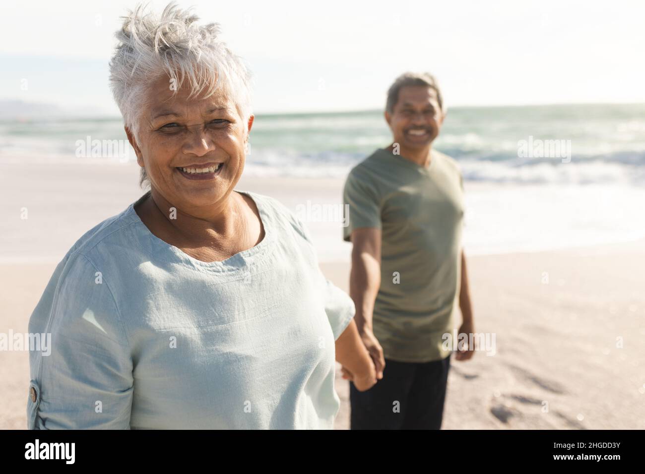 Porträt einer lächelnden älteren multirassischen Frau, die an einem sonnigen Tag am Strand Hand mit dem Mann hält Stockfoto