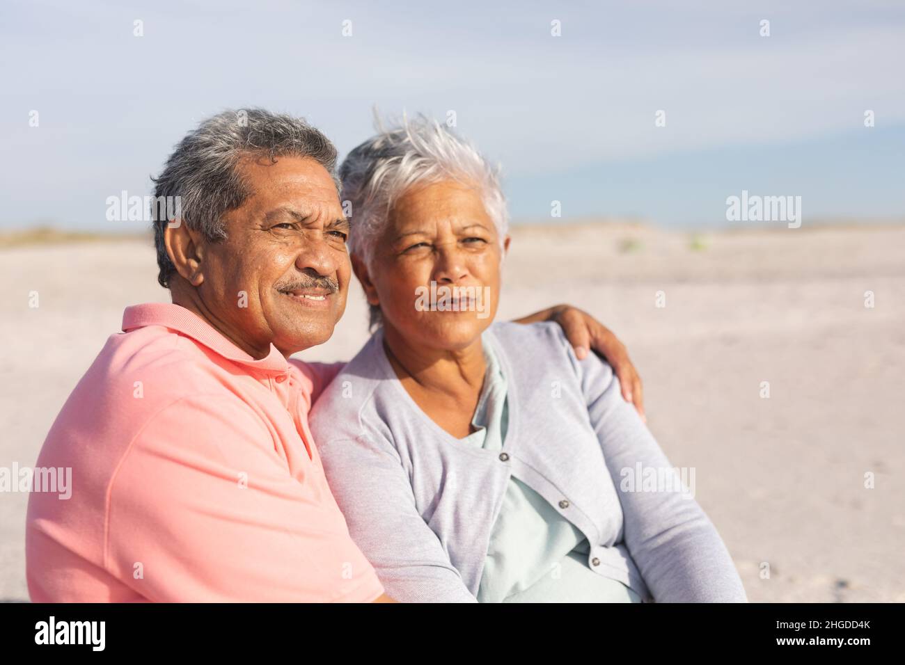 Nachdenkliches, multirassisches Seniorenpaar, das sich an einem sonnigen Tag am Strand entspannt Stockfoto