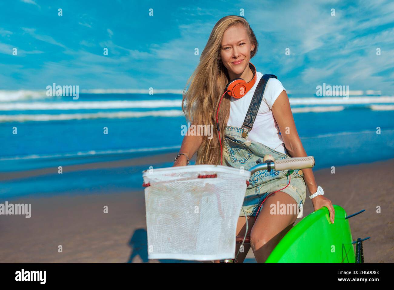 Junge Frau mit Surfbrett und Fahrrad am Strand. Stockfoto