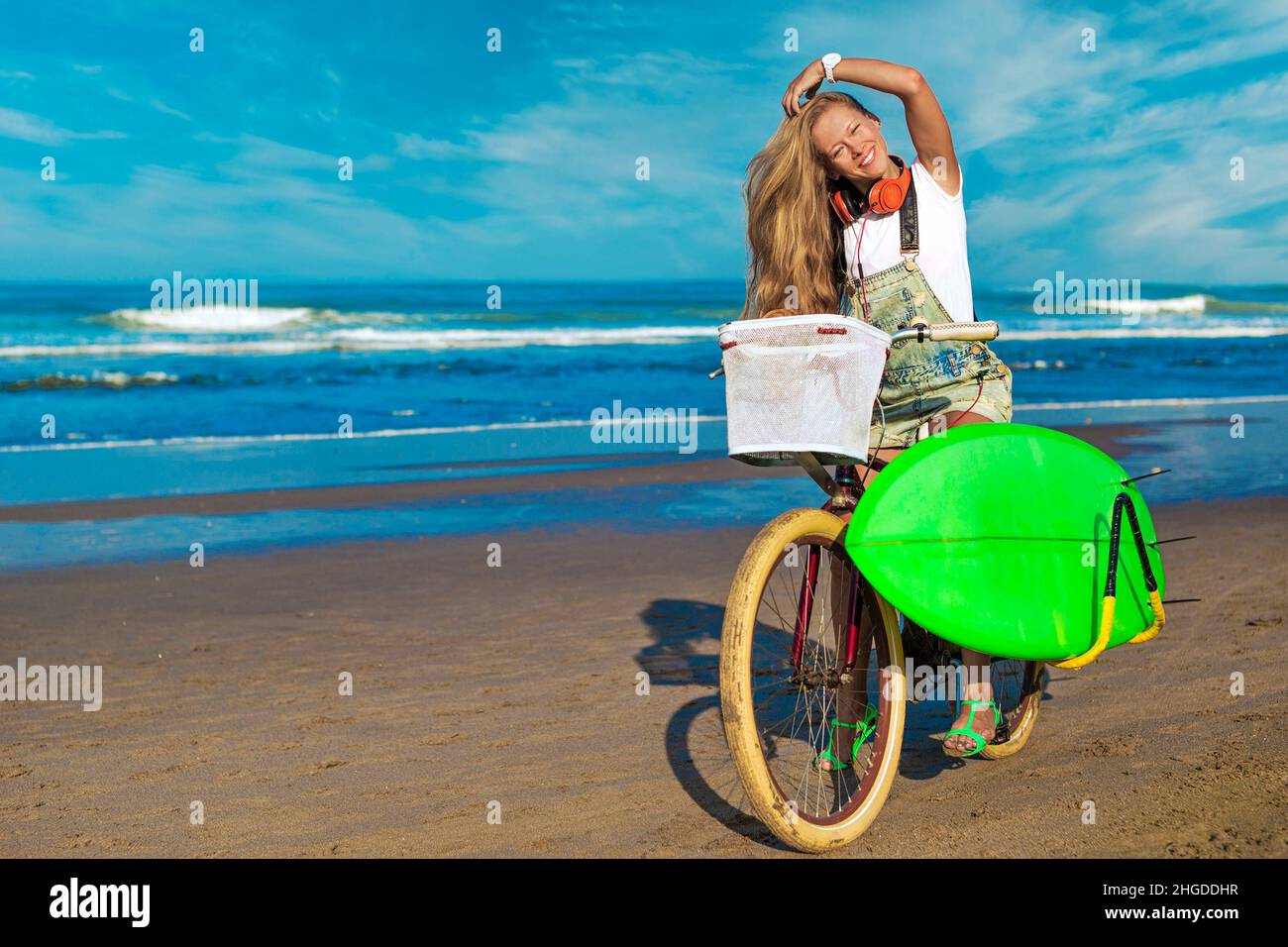 Junge Frau mit Surfbrett und Fahrrad am Strand. Stockfoto